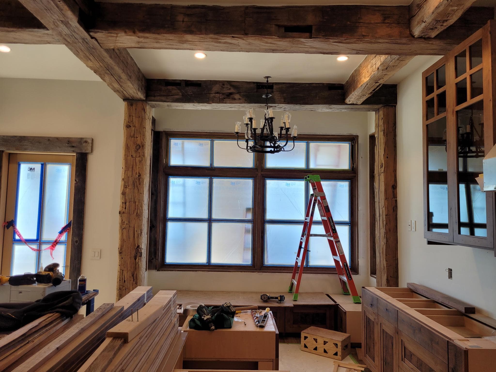 Great room with timber framing, large windows, and kitchen cabinetry under construction