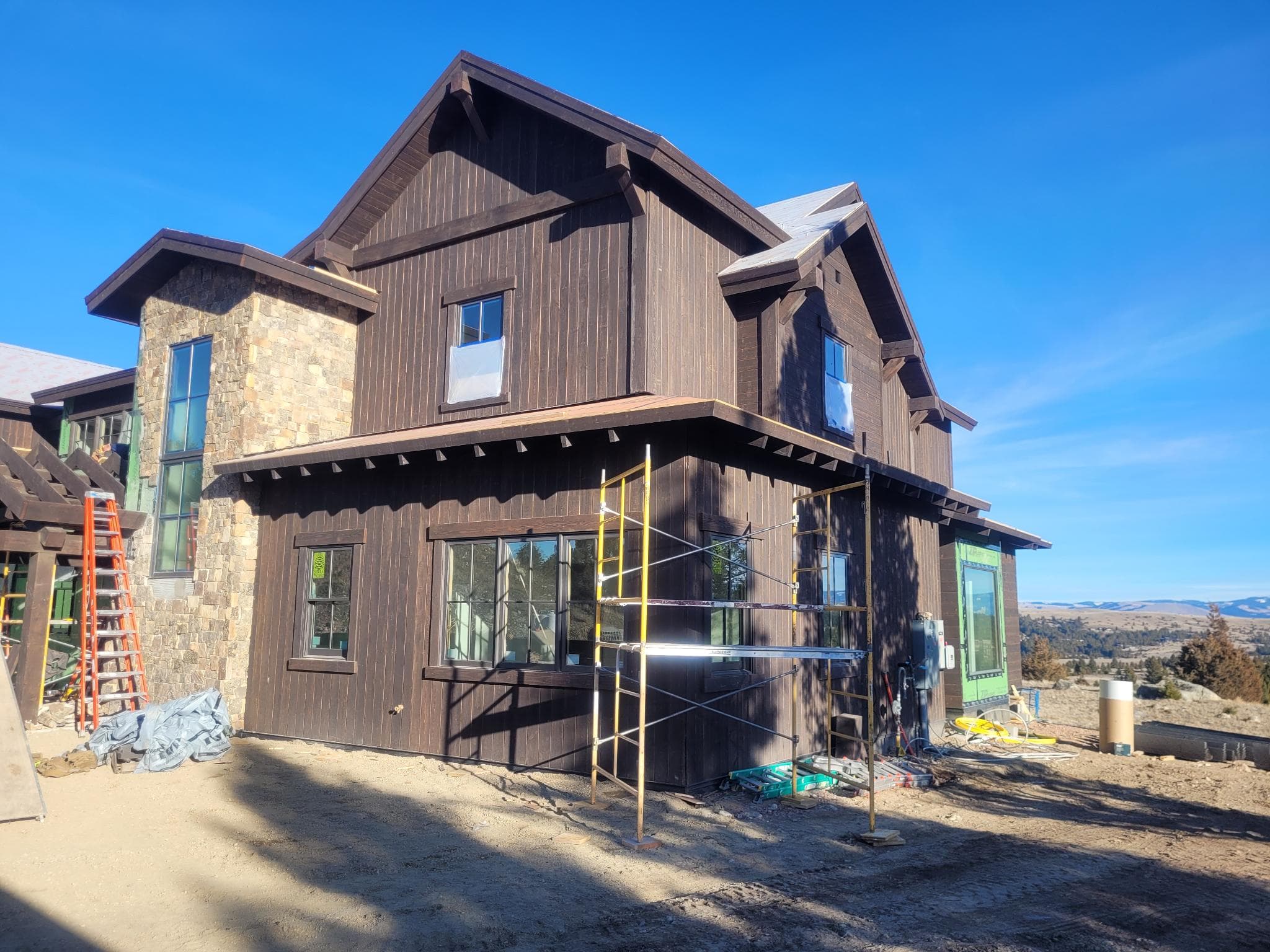 Custom mountain home under construction with dark wood siding and natural stone accents
